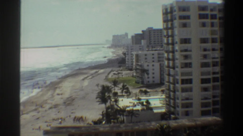 8mm footage circa 1975 of a Florida beachfront resort from a high vantage point, featuring apartment towers, a pool complex, and beach.