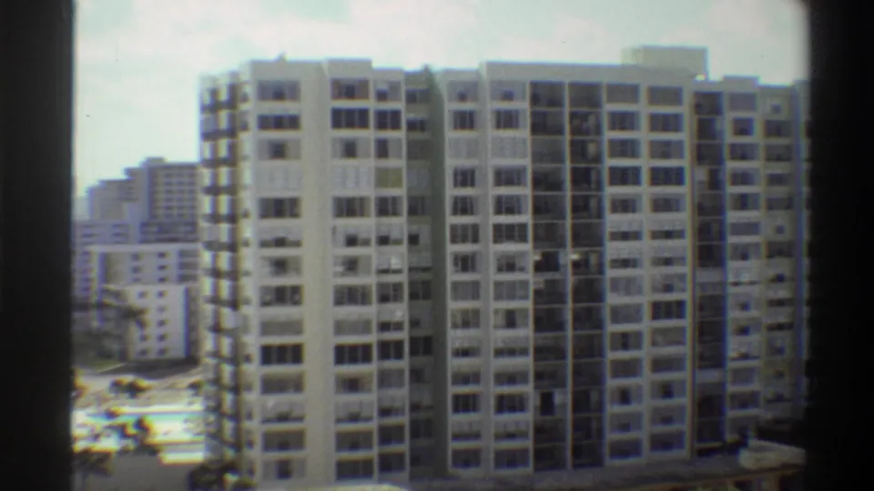 8mm frame ca. 1975: two Florida beachfront high-rise towers fill the frame with sandy beach, ocean, and palm trees visible to the left.