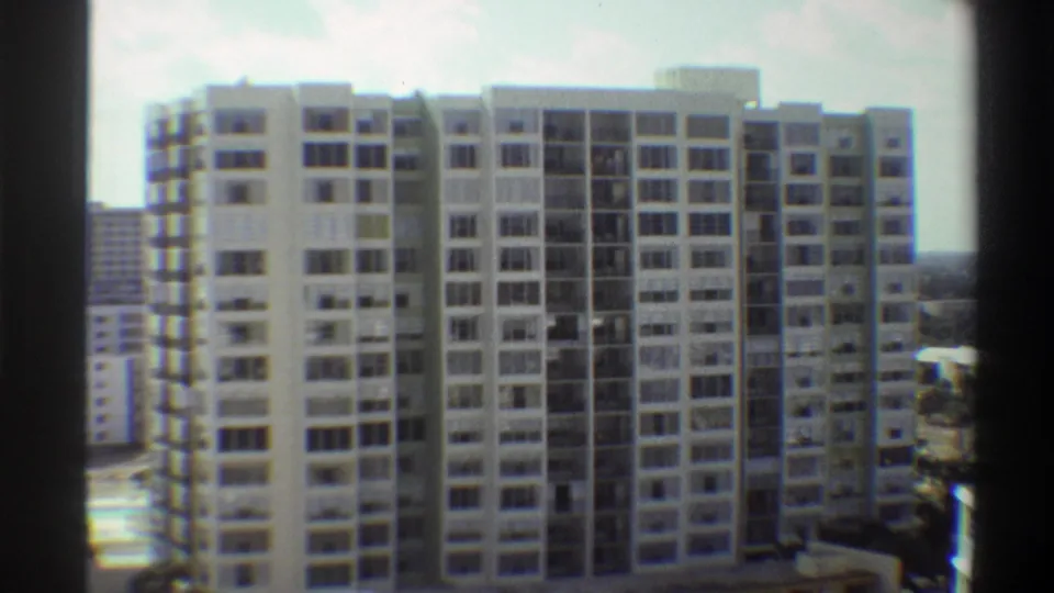 8mm home movie frame, circa 1975, showing a tall mid-century modernist apartment building in Gainesville, Florida, shot from a neighbouring elevated vantage point.
