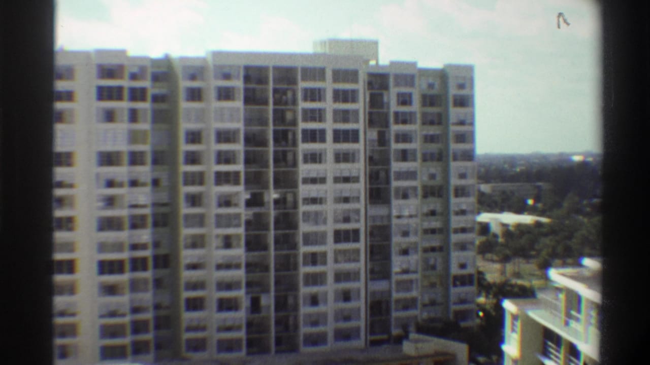 8mm frame circa 1975 of a multi-storey Gainesville, Florida apartment building; subtle pan shows lower adjoining structure and subtropical tree canopy.