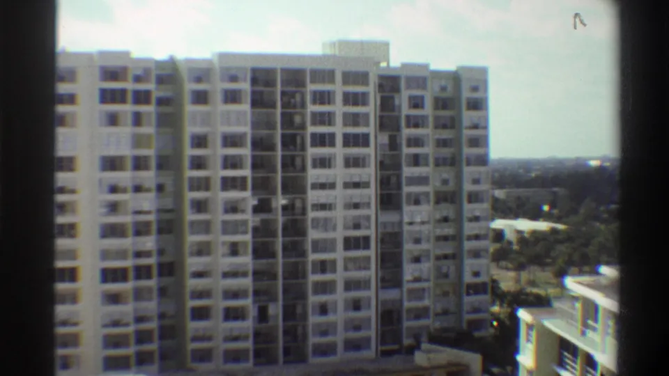8mm frame circa 1975 of a multi-storey Gainesville, Florida apartment building; subtle pan shows lower adjoining structure and subtropical tree canopy.