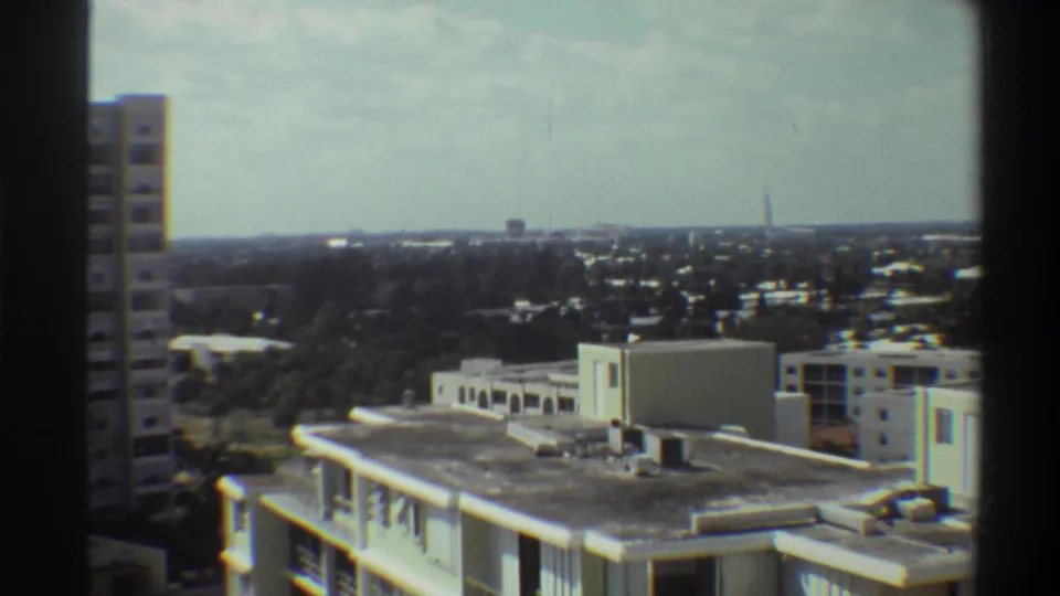 Super 8 frame from 1975 Gainesville, Florida: rooftop mechanical equipment in foreground, tree-covered city panorama, and a faint antenna on the distant horizon.