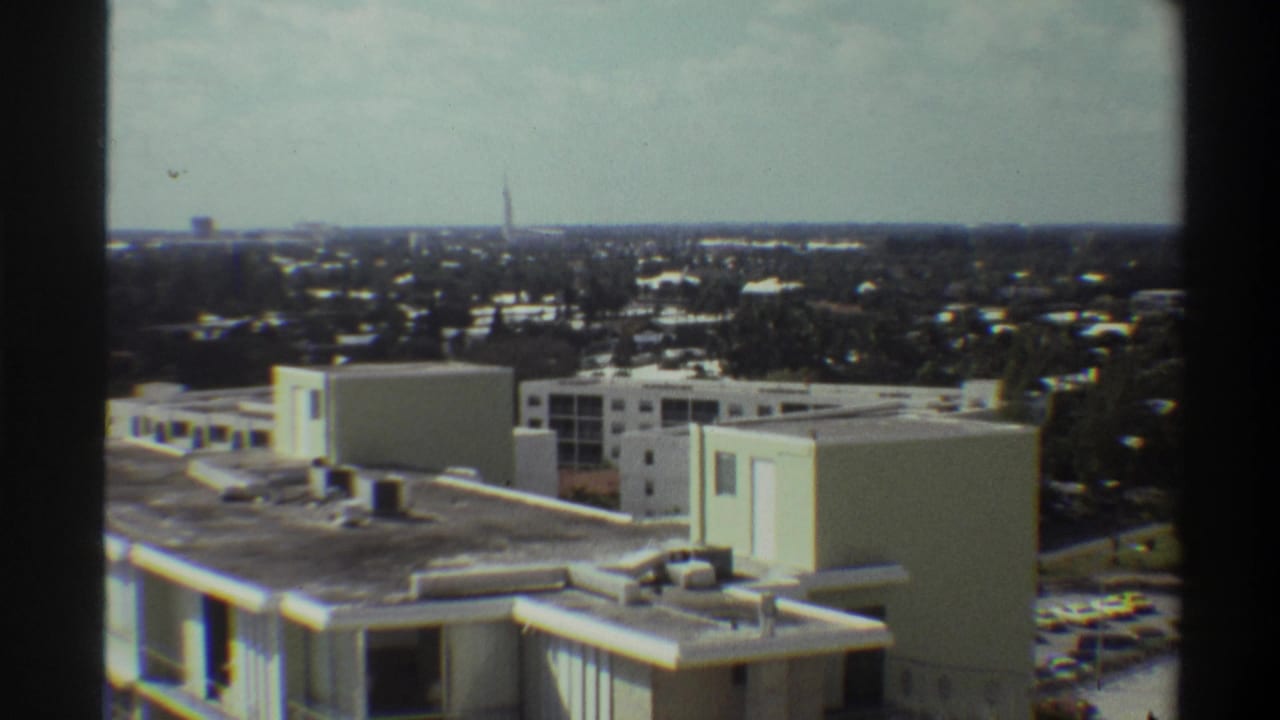 Elevated rooftop view over mid-century buildings, Gainesville, Florida, circa 1975; parking area with 1970s-era cars visible at right edge.