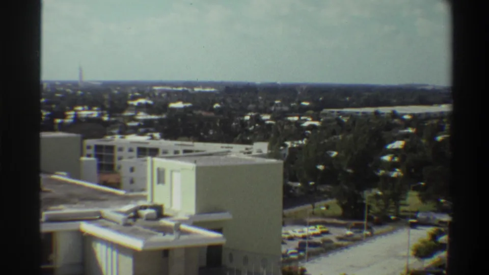 Final frame of elevated survey over what appears to be Gainesville, Florida, circa 1975; institutional rooftop, parking area, and subtropical canopy extending to horizon.