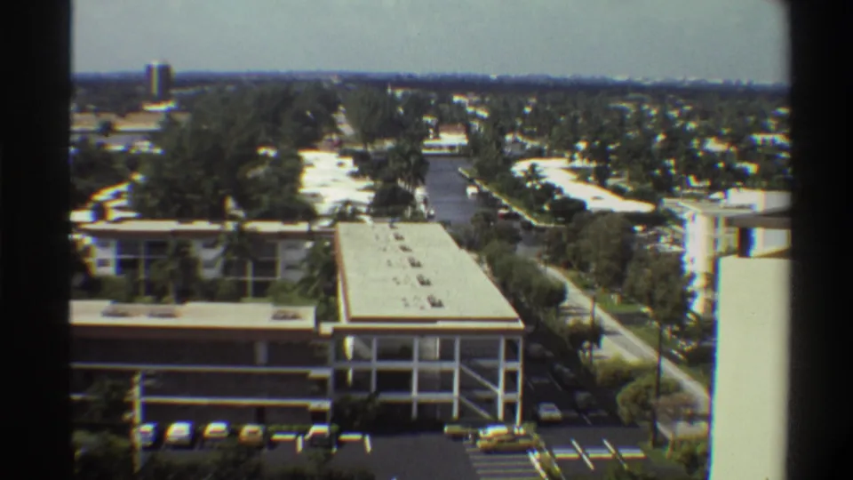 8mm footage circa 1975 showing a static elevated perspective over a low-rise building, parking lot, subtropical vegetation, and flat Florida suburban landscape.