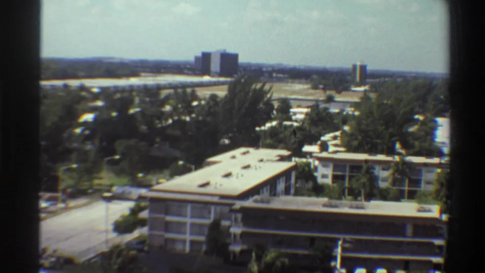 End-of-pan 8mm frame of 1970s Gainesville, Florida institutional complex and surrounding suburban tree canopy with distant towers.