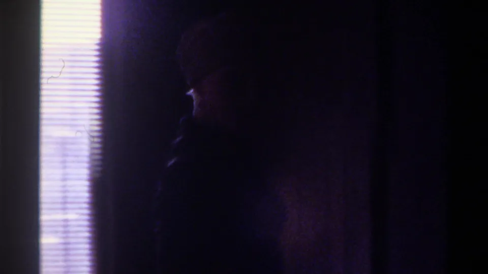 Woman largely silhouetted against backlit window blinds, beginning to turn toward camera in a domestic interior, circa 1975 Gainesville, Florida, 8mm home movie.