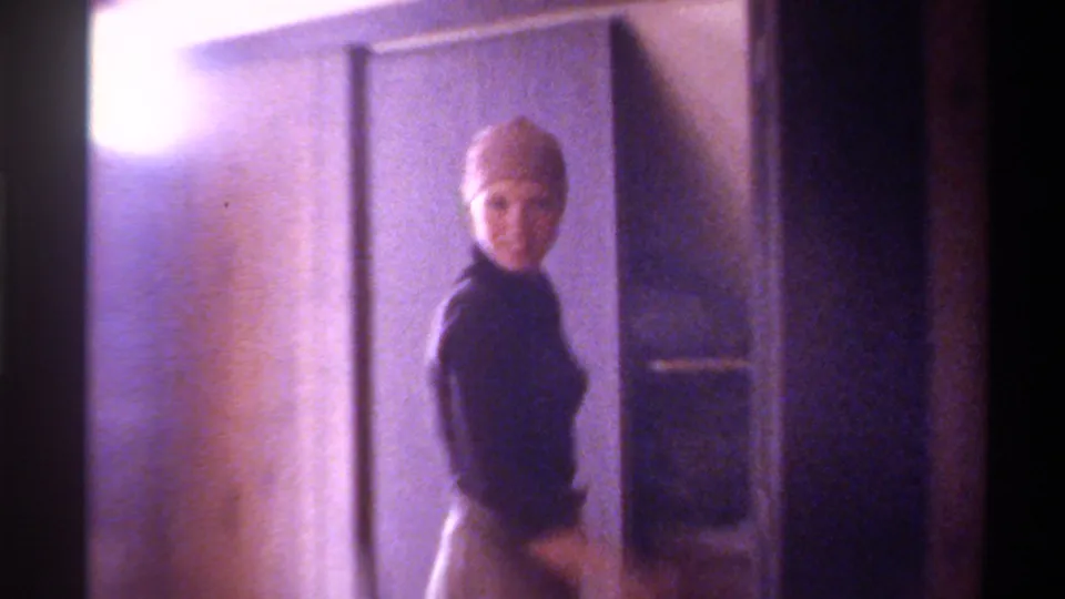 Woman in black turtleneck and light high-waisted skirt poses full-length in a 1970s home interior with visible film light flare, circa 1975, Florida.