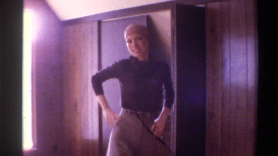 Woman in 1970s black turtleneck and light skirt poses with hand on hip in a private interior beside wall paneling, circa 1975, Florida.