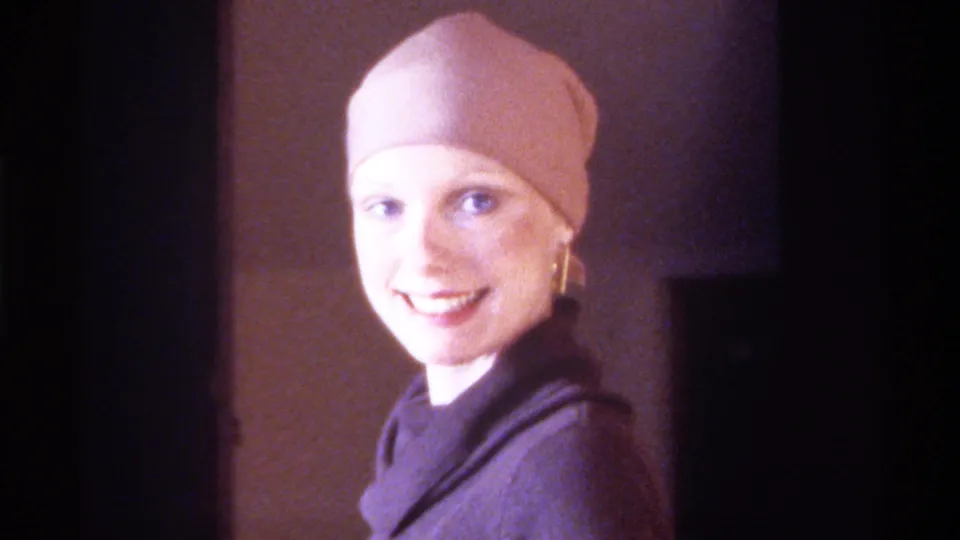 8mm home movie, circa 1975, Gainesville, Florida: sustained close-up of woman smiling toward camera, beige fitted cap and gold drop earrings, warm 8mm grain and color.