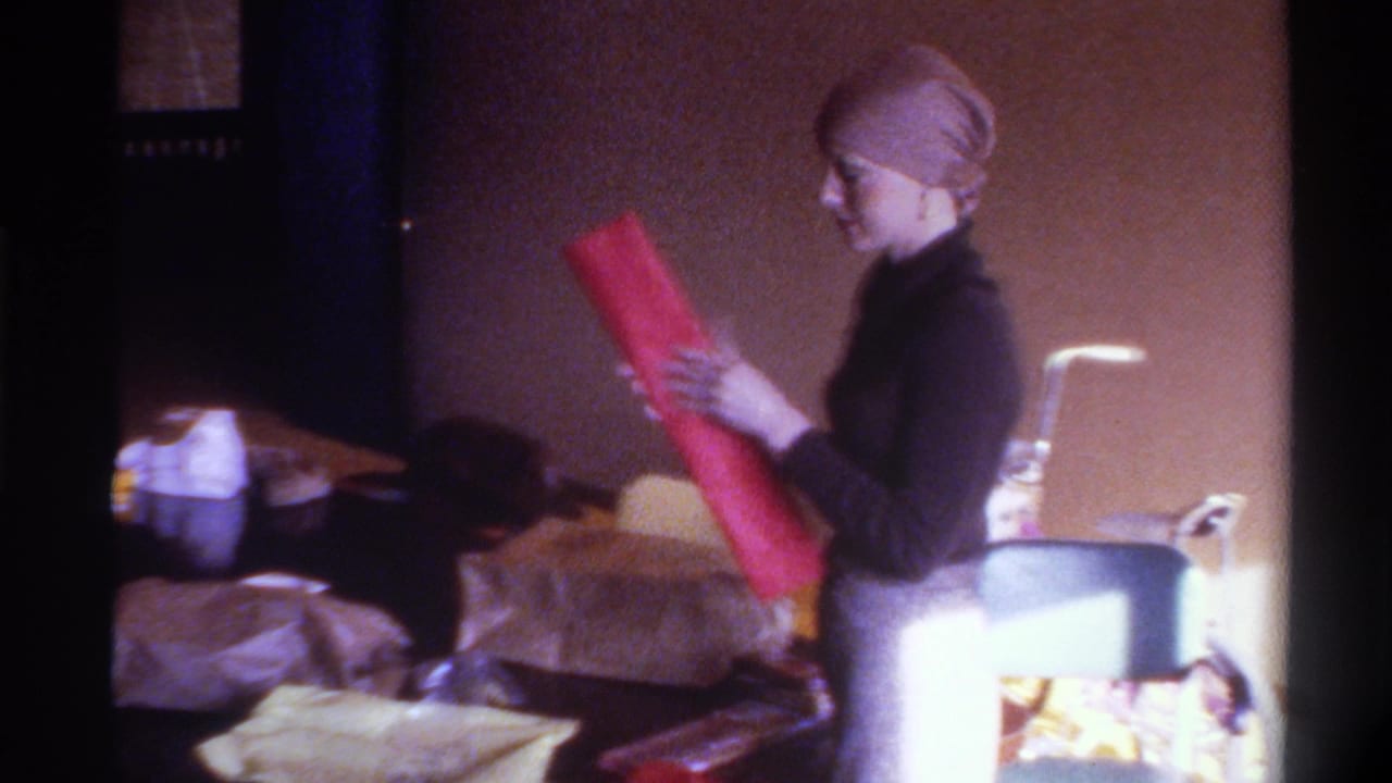 Woman in three-quarter profile holds a long sheet of red wrapping paper aloft; glasses visible on her face.
