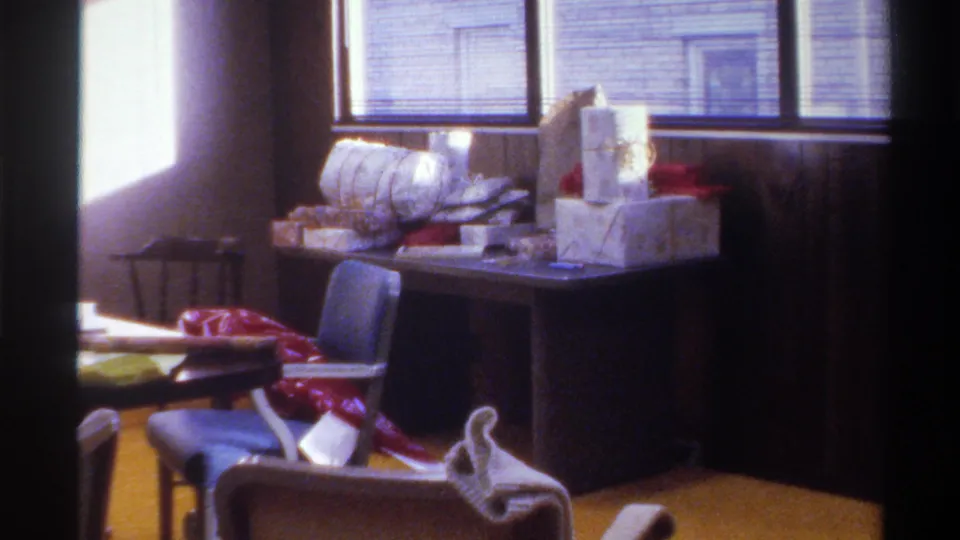 Desk piled with wrapped Christmas presents and ribbon in wood-paneled room, no person visible, 8mm home movie, Gainesville Florida, circa 1975