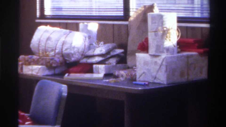 Interior view from a 1975 Gainesville, Florida home movie: Christmas gifts on dark table, blue upholstered chair prominent, red wrapping at right, wood-panel walls.