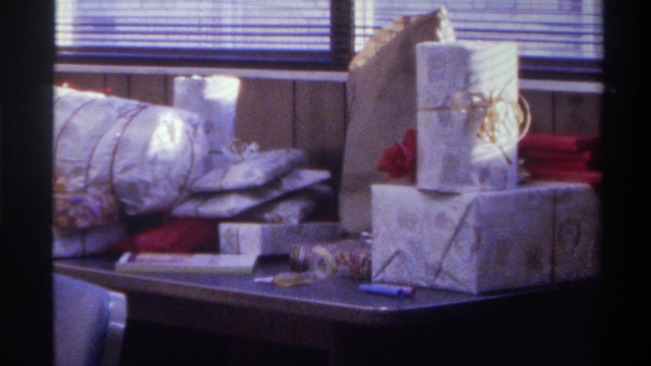 Wrapped gifts piled on a dark table with horizontal venetian blinds in background; Gainesville, Florida, 1975, 8mm home movie.