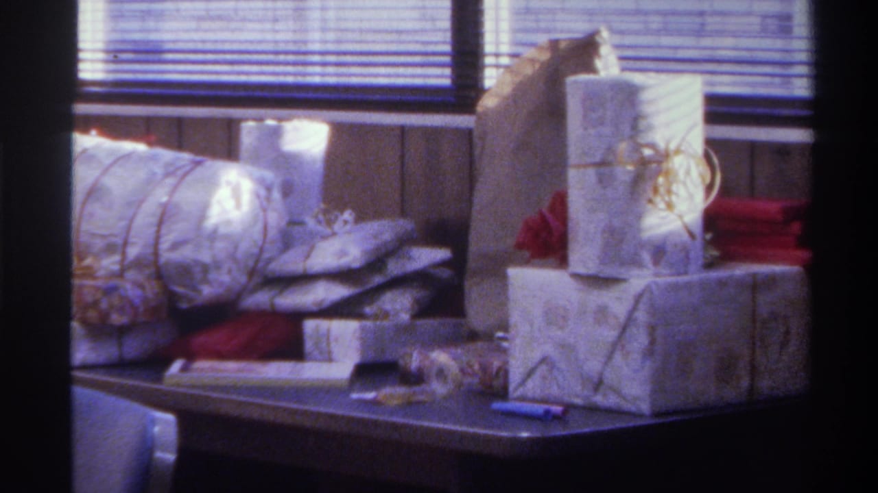 Static shot of wrapped gifts on dark table with backlit venetian blinds; Gainesville, Florida, 1975, 8mm home movie.