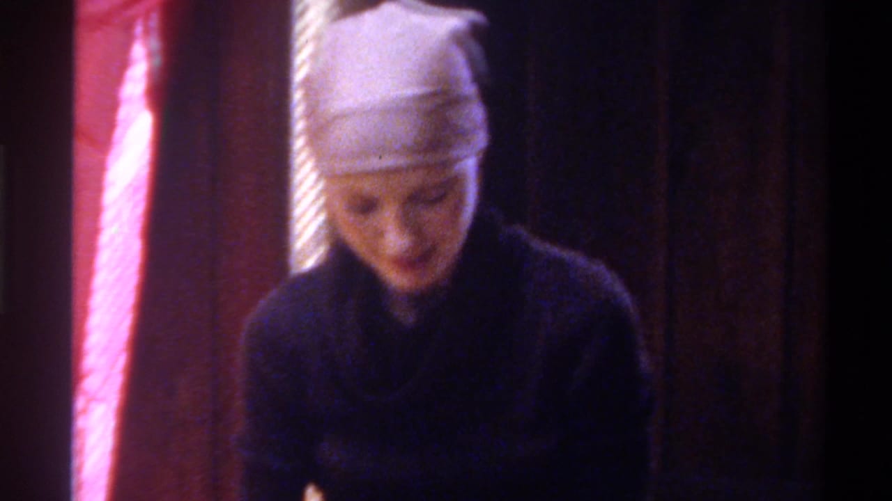 Young woman in dark cowl-neck sweater and head wrap looks downward at a craft project; pink draped fabric fills the background; Gainesville, Florida, circa 1975.
