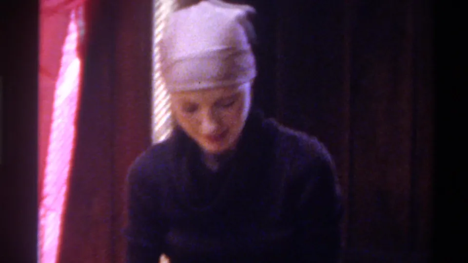 Young woman in dark cowl-neck sweater and head wrap looks downward at a craft project; pink draped fabric fills the background; Gainesville, Florida, circa 1975.