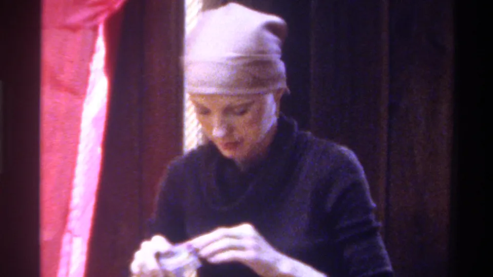 Woman lifts her hands to handle a small object — possibly tape or material — in a private interior; circa Gainesville, Florida, 1975.