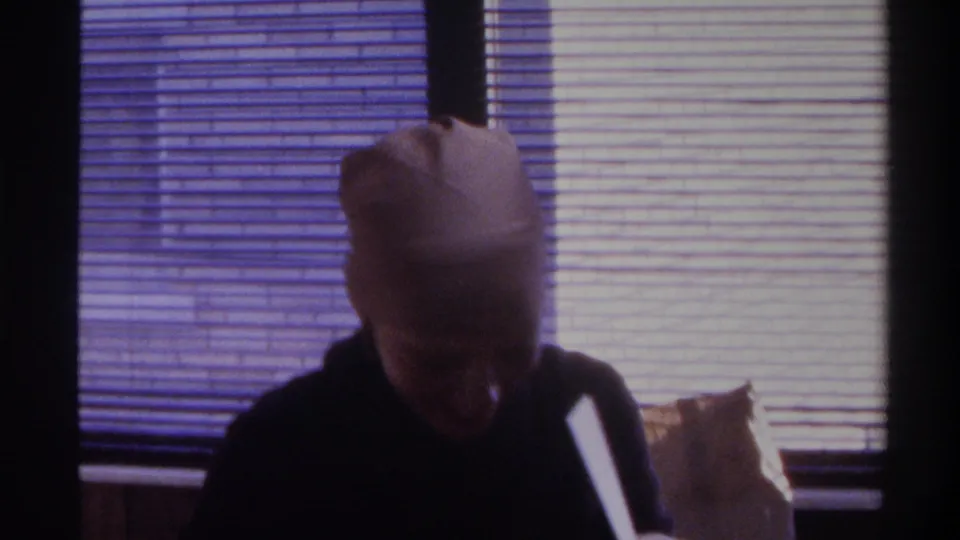 Woman in brown headscarf with face obscured — head bowed or covering adjusted — in sunlit room with horizontal blinds, Gainesville, Florida, circa 1975 home movie.