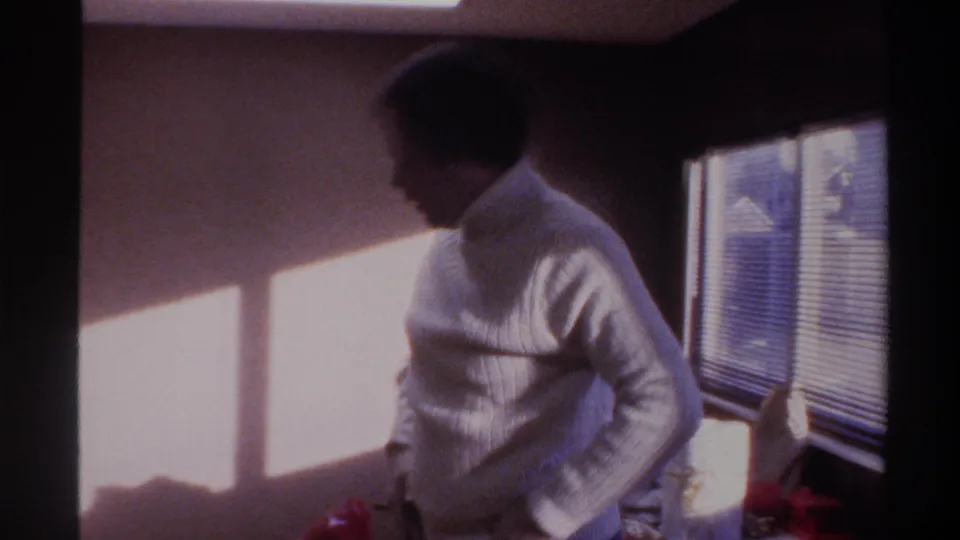 Man in white ribbed turtleneck turned in profile inside a domestic room with Venetian blinds, 8mm home movie, Gainesville, Florida, circa 1975.