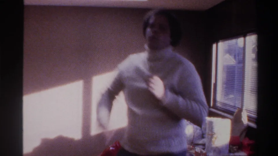 Heavyset man in white ribbed turtleneck adjusting his sweater, facing camera in warm 8mm home movie footage, Gainesville, Florida, circa 1975.