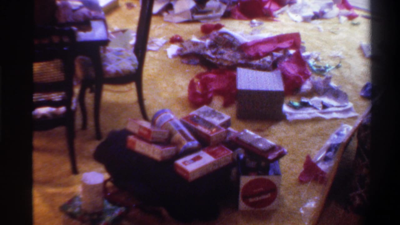 8mm home movie still, circa 1975, Gainesville Florida: gift boxes and red ribbons scattered across a light-colored carpet after Christmas morning gift opening.