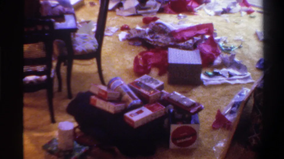 8mm home movie still, circa 1975, Gainesville Florida: gift boxes and red ribbons scattered across a light-colored carpet after Christmas morning gift opening.