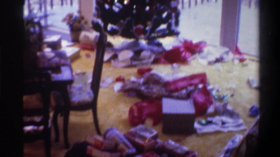 8mm home movie still, circa 1975, Gainesville Florida: living room floor after gift opening, Christmas tree partially visible at left, ribbons and open boxes across the carpet.