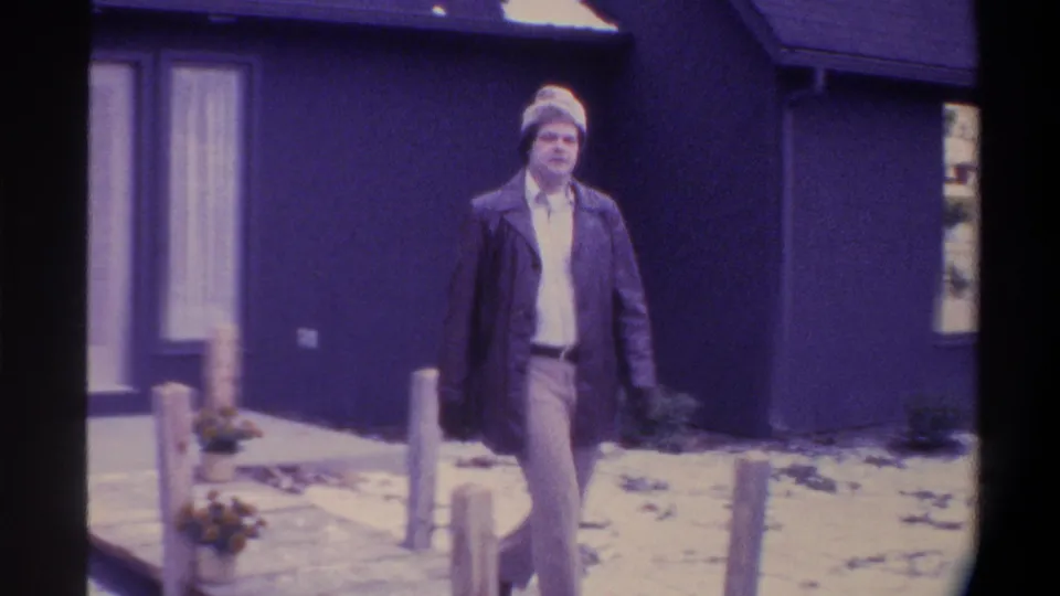 Man in dark overcoat and knit hat walks toward camera along a snowy path with wooden post bollards, Gainesville, Florida, circa 1975.