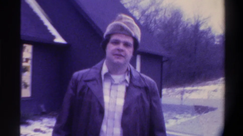 Close shot of a smiling man in 1970s winter clothing, bare winter tree and dark blue building in background, Gainesville, Florida, circa 1975.
