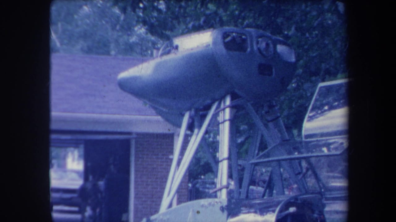 Aircraft cockpit nose on tripod stand in driveway with figure near garage doorway, Yucaipa California ca. 1959, aged 8mm film.