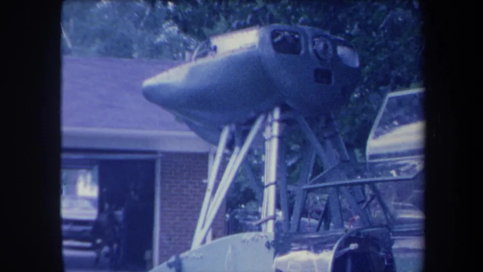 Aircraft nose/cockpit on metal tripod at lower camera angle, residential driveway in Yucaipa California ca. 1959, blue-shifted 8mm.