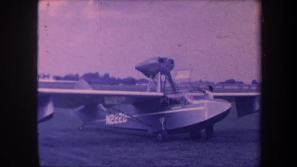 8mm home movie still, circa 1959, Yucaipa California airfield; single-engine amphibious aircraft N2220 with figure visible near cockpit opening.