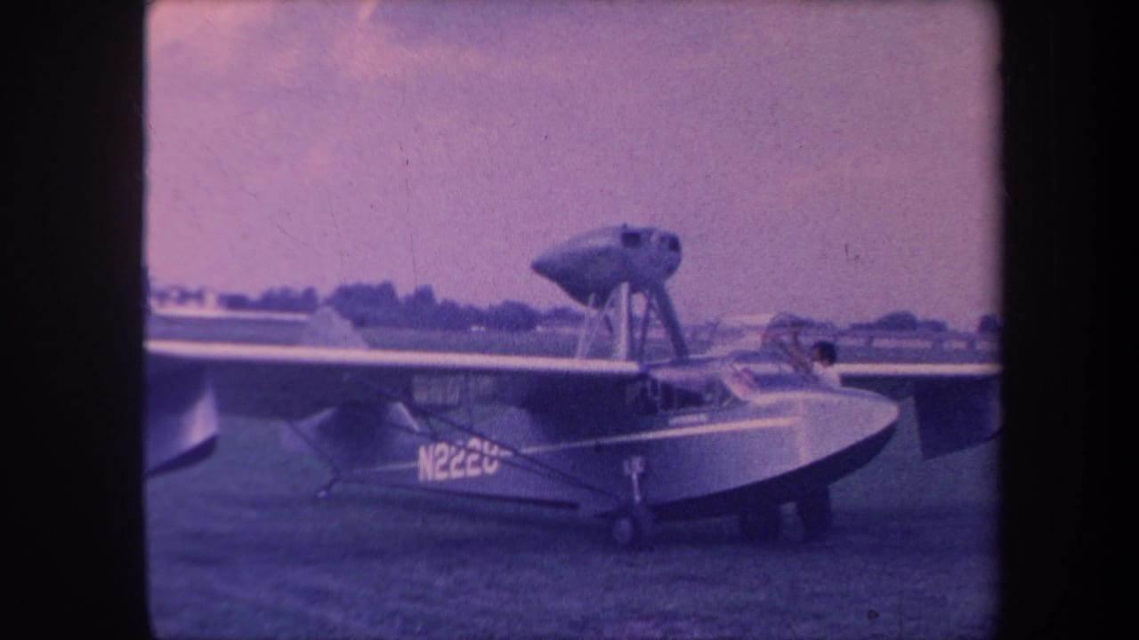 8mm home movie still, circa 1959, Yucaipa California; amphibious aircraft N2220 on airfield grass with figure at cockpit in pre-flight activity.