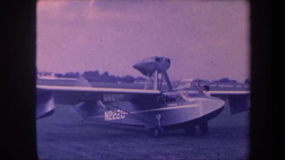 8mm home movie still, circa 1959, Yucaipa California; amphibious aircraft N2220 on airfield grass with figure at cockpit in pre-flight activity.