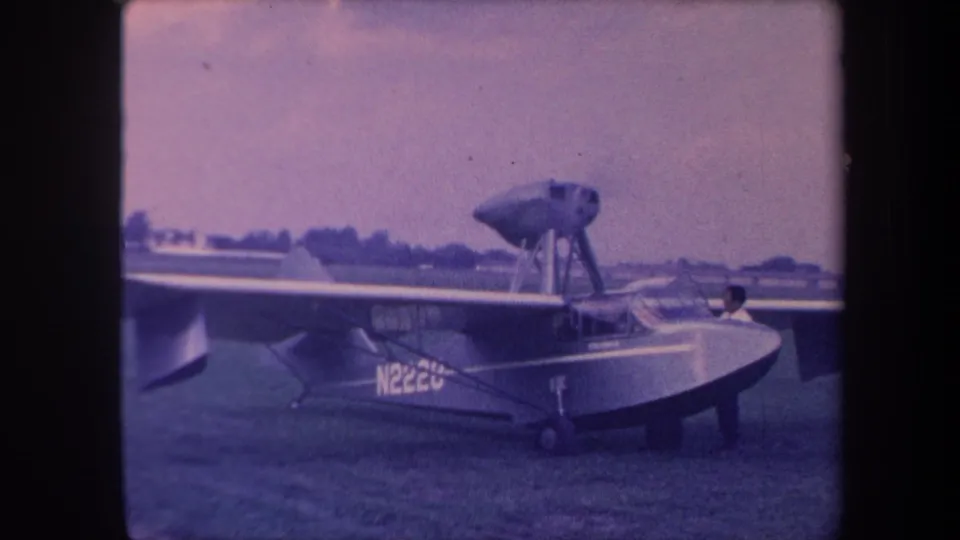 8mm home movie still, circa 1959, Yucaipa California; single-engine amphibious aircraft N2220 with occupant at cockpit, consistent with engine-start sequence.