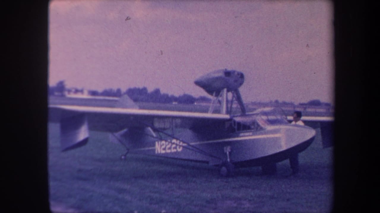 Amphibious aircraft with boat-hull fuselage and registration N222U on grass airfield, 8mm color film with blue cast.