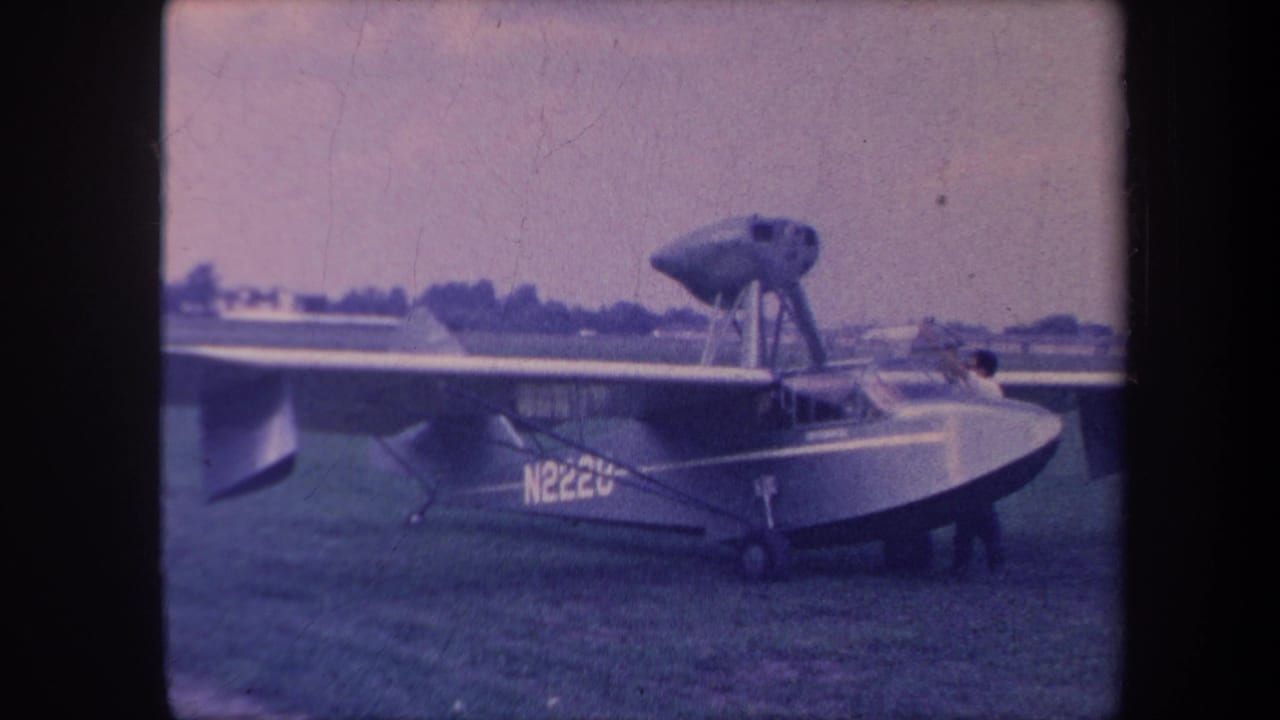 Amphibious flying boat with registration N222U on grass field, front-quarter view, blue-shifted 8mm film.