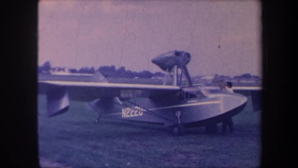 Amphibious flying boat N222U on grass airfield, California circa 1959; high-mounted wing and tractor propeller clearly visible, 8mm color film.