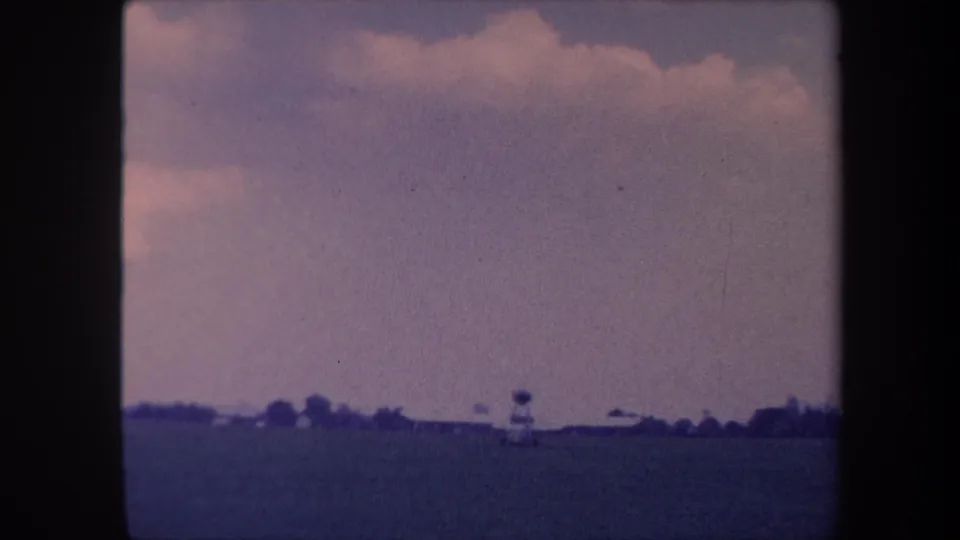 Wide ground-level view of a grass airstrip near Yucaipa, California, circa 1959, showing a small aircraft at the far horizon beneath cumulus clouds.
