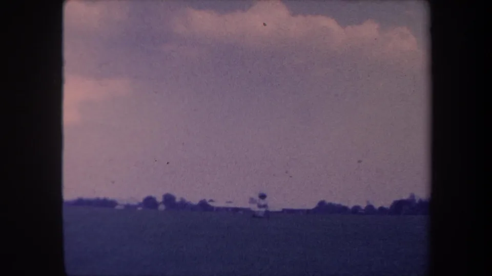 Small propeller aircraft near a tower-like structure at the edge of a grass airstrip, Yucaipa, California area, circa 1959, filmed on 8mm with visible color aging.
