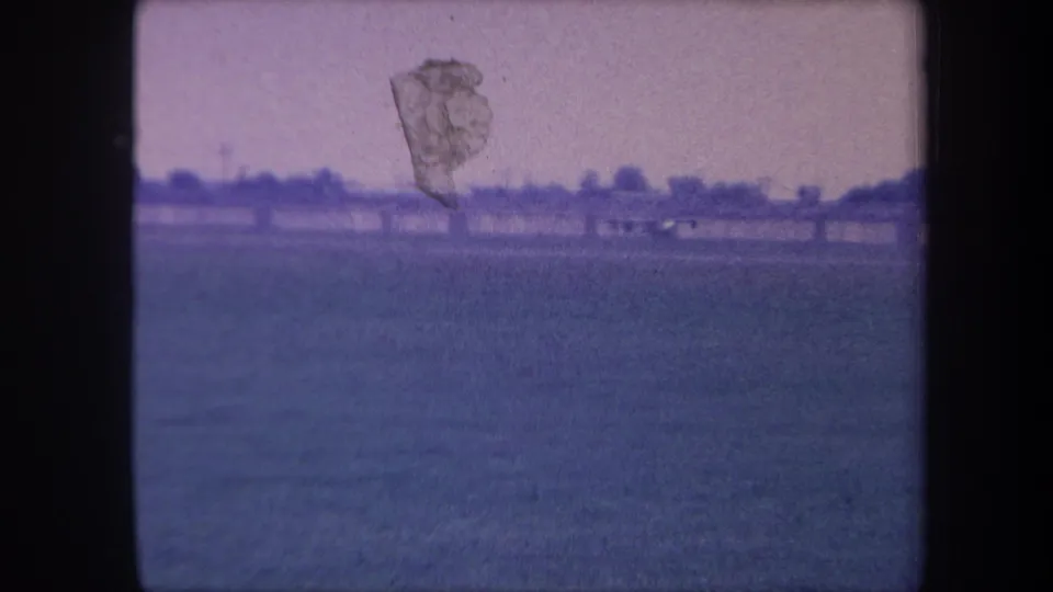 8mm home movie frame circa 1959, Yucaipa, California: small plane just airborne over a flat rural airstrip, with visible emulsion damage and blue-purple color shift.