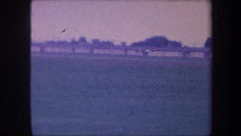 8mm home movie frame circa 1959, Yucaipa, California: small plane receding into the distance over a flat rural airstrip under an aged, blue-shifted sky.