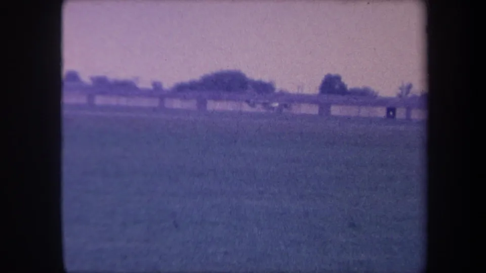 8mm home movie frame, circa 1959, showing a flat grass airfield in the Yucaipa, California area; low structures and trees at horizon.