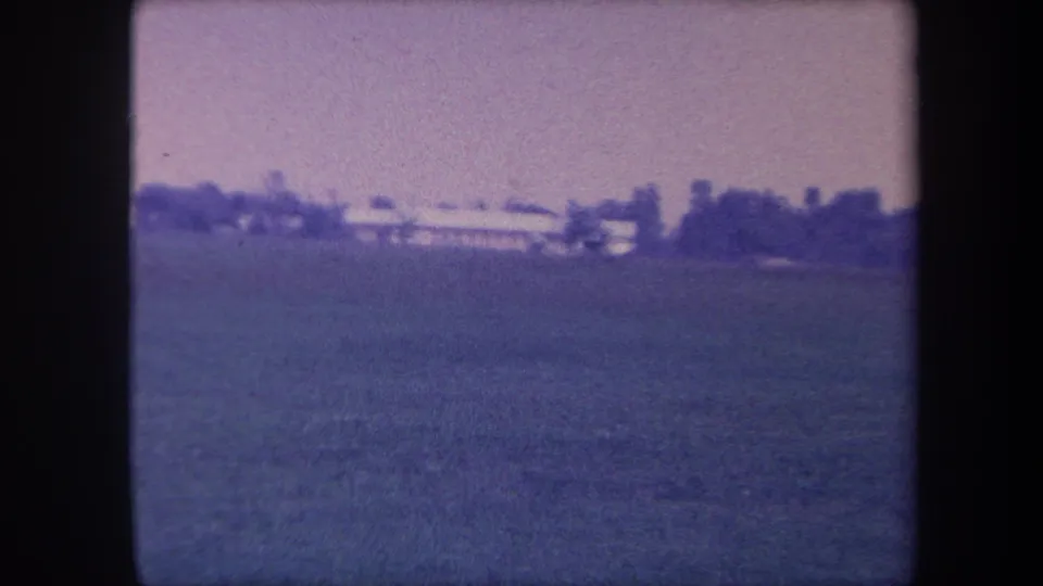 Closing frame of the 1959 Yucaipa rural sequence — open field, low buildings, and treeline under a washed-out sky with heavy purple-blue emulsion fade.