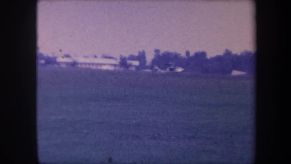 Wide establishing shot of a grass airfield, possibly near Yucaipa, California, circa 1959; no aircraft yet visible; strong purple color cast from aged 8mm film.