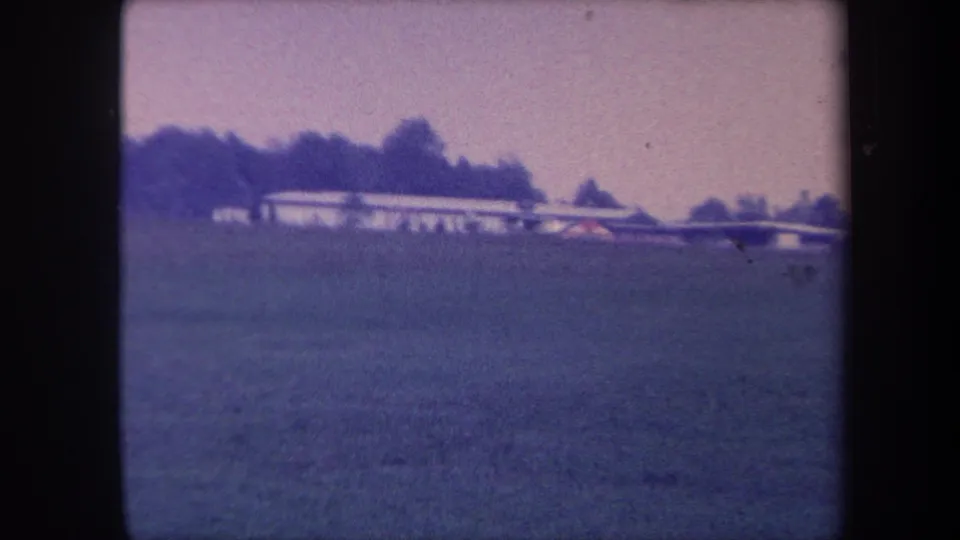 Small single-engine aircraft moving across the frame above a grass airfield near Yucaipa, California, circa 1959; lavender color cast and film grain visible throughout.