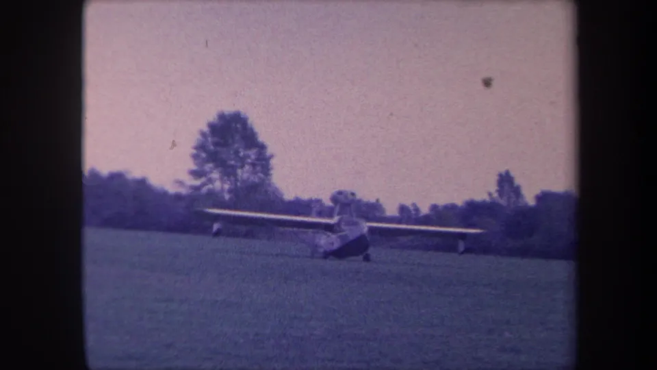 Light single-engine aircraft on a grass strip, possibly moments after landing, Yucaipa, California, circa 1959; 8mm film with purple color shift and grain.