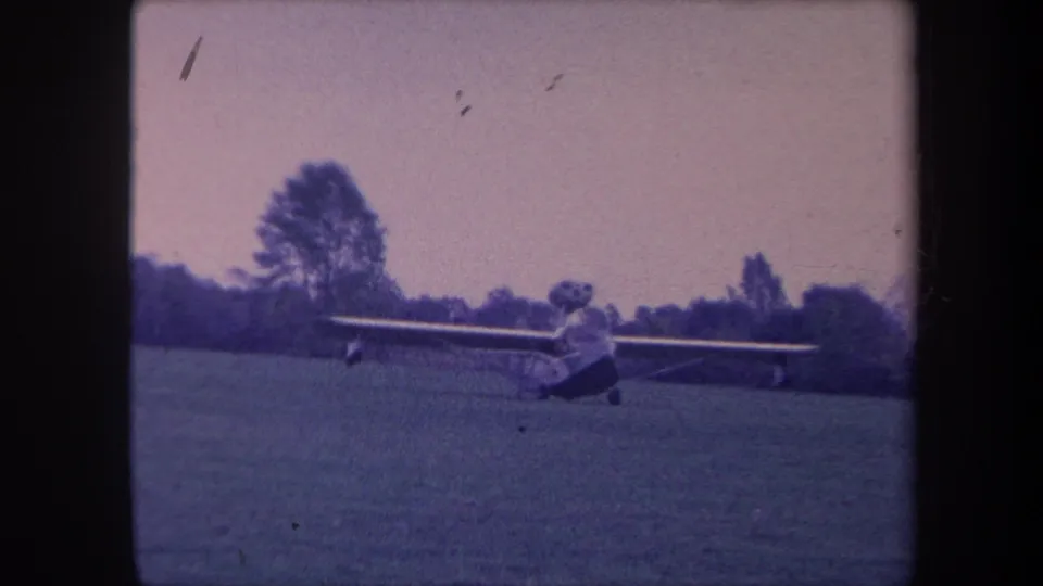 Light aircraft on a grass strip, Yucaipa, California, circa 1959; 8mm footage with notable surface debris, scratch marks, and purple color shift.