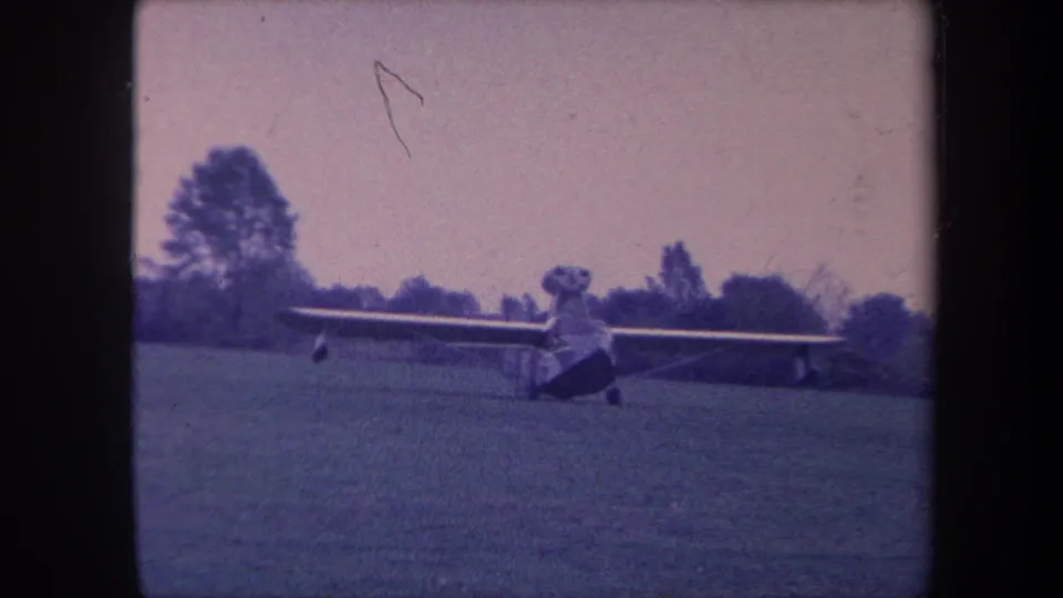 Light aircraft on a grass airfield, Yucaipa, California, circa 1959; a diagonal scratch artifact is prominent in the upper frame on this aged 8mm film.
